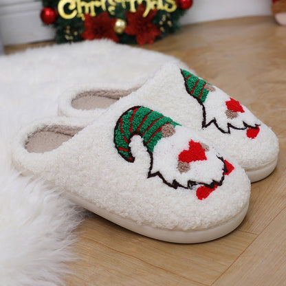 Chaussons de Noël Doudounea en peluche blanche avec motif lutin festif, semelle confortable, ambiance chaleureuse avec décoration de Noël en arrière-plan