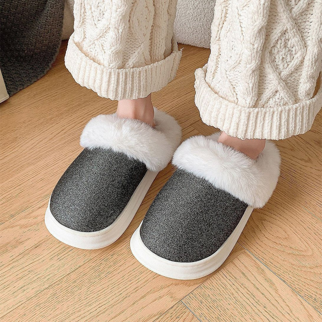 Chaussons d'hiver Doudounea gris avec bordure en fourrure blanche, portés avec un pantalon en tricot blanc, sur un parquet en bois chaleureux